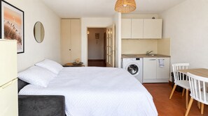 A bedroom with a bed, a bedside table, a mirror, and a wardrobe. There is a kitchenette with a washing machine, a sink, and a small dining table with chairs. - Air-conditioned studio with a balcony, parking, and the beach 300 meters away in Sainte-Maxime (Sainte-Maxime)