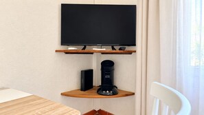 A flat-screen TV mounted on a wall above a wooden shelf with a coffee maker and a speaker. - Air-conditioned studio with a balcony, parking, and the beach 300 meters away in Sainte-Maxime (Sainte-Maxime)