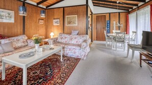 Un saló agradable amb sostre de fusta, un sofà floral, una taula de cafè blanca i una zona de menjador amb taula i cadires.