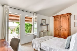 Quarto com cama, guarda-roupa de madeira e vista para o jardim através de uma porta aberta.
