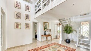 Ein geräumiges Foyer mit hoher Decke, einer Treppe, einem gemusterten Teppich und gerahmten Kunstwerken an den Wänden.