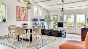 Ein Essbereich mit rundem Tisch, Stühlen und Teppich; ein Wohnzimmer mit Sofa und Fernseher; und große Fenster mit Blick.