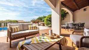 Eine Terrasse im Freien mit einer Couch, Stühlen, einem Tisch und Blick aufs Meer.