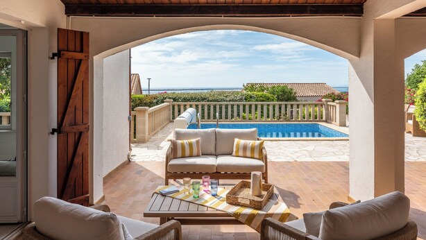 Eine möblierte Terrasse mit einer Sitzecke, einem Tisch mit Gläsern und Blick auf einen Swimmingpool.