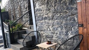 A patio area with a stone wall, a wooden door, and two black wire chairs around a small wooden table. - Imperio vert adventure with a view (Tabua)