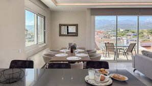 A dining area with a table set for six, a large window with a mountain view, and a balcony with outdoor seating. - Ardians Home, Be on Holidays (Chania)