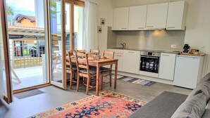 A modern kitchen with white cabinets, a dining area with a wooden table and chairs, and a grey sofa. - Appartment sulle Viti by Interhome (Losone)