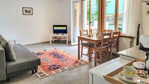 A modern living room with a sofa, a dining table with chairs, a TV on a stand, and a large window with curtains. - Appartment sulle Viti by Interhome (Losone)
