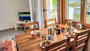 A dining area with a wooden table set for breakfast, a television on a stand, and a view of the outdoors through large windows. - Appartment sulle Viti by Interhome (Losone)