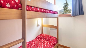 A bunk bed with a red floral bedspread, a window with a blue curtain, and a white wall with a thermostat.