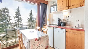 A compact kitchen with wooden cabinets, a microwave, and a sink. There's a table with chairs and a view of trees outside.