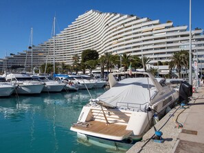 Un puerto deportivo con yates amarrados, un edificio moderno grande con balcones y palmeras.