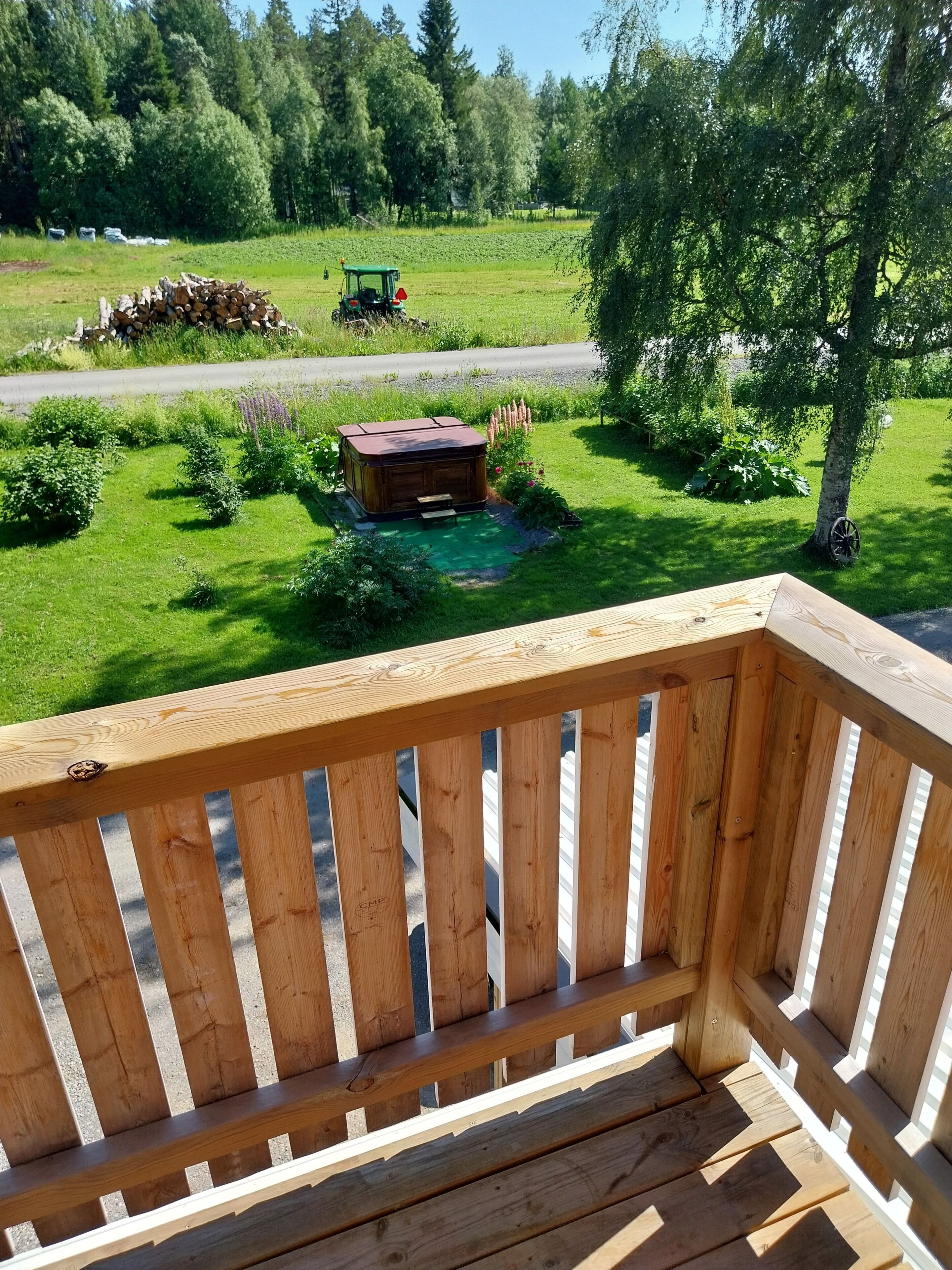 Terraza de madera con vistas a un jardín y una carretera.