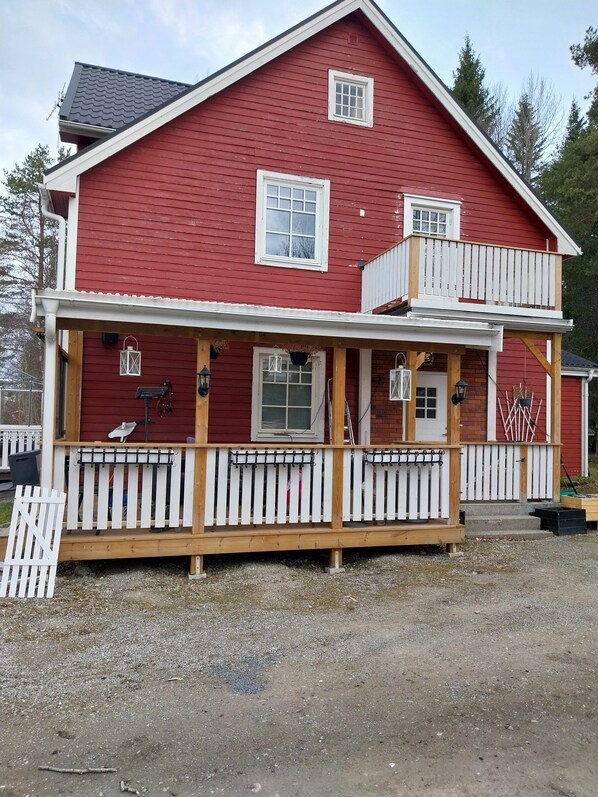 A two-story red house with a balcony, a covered porch, and a small front yard.