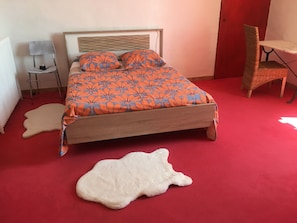 En seng med et orange blomstret sengetæppe, en hvid, blød måtte og et rødt tæppegulv.