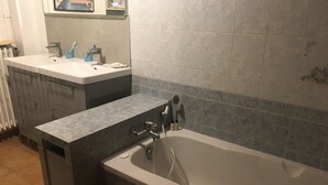 Un baño con bañera, lavabo y tocador. Hay escalones que llevan a la bañera, y se ve un perchero.