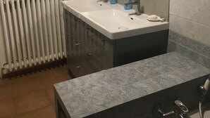 Un baño moderno con un lavamanos blanco, muebles oscuros, un espejo grande y una encimera de mármol.