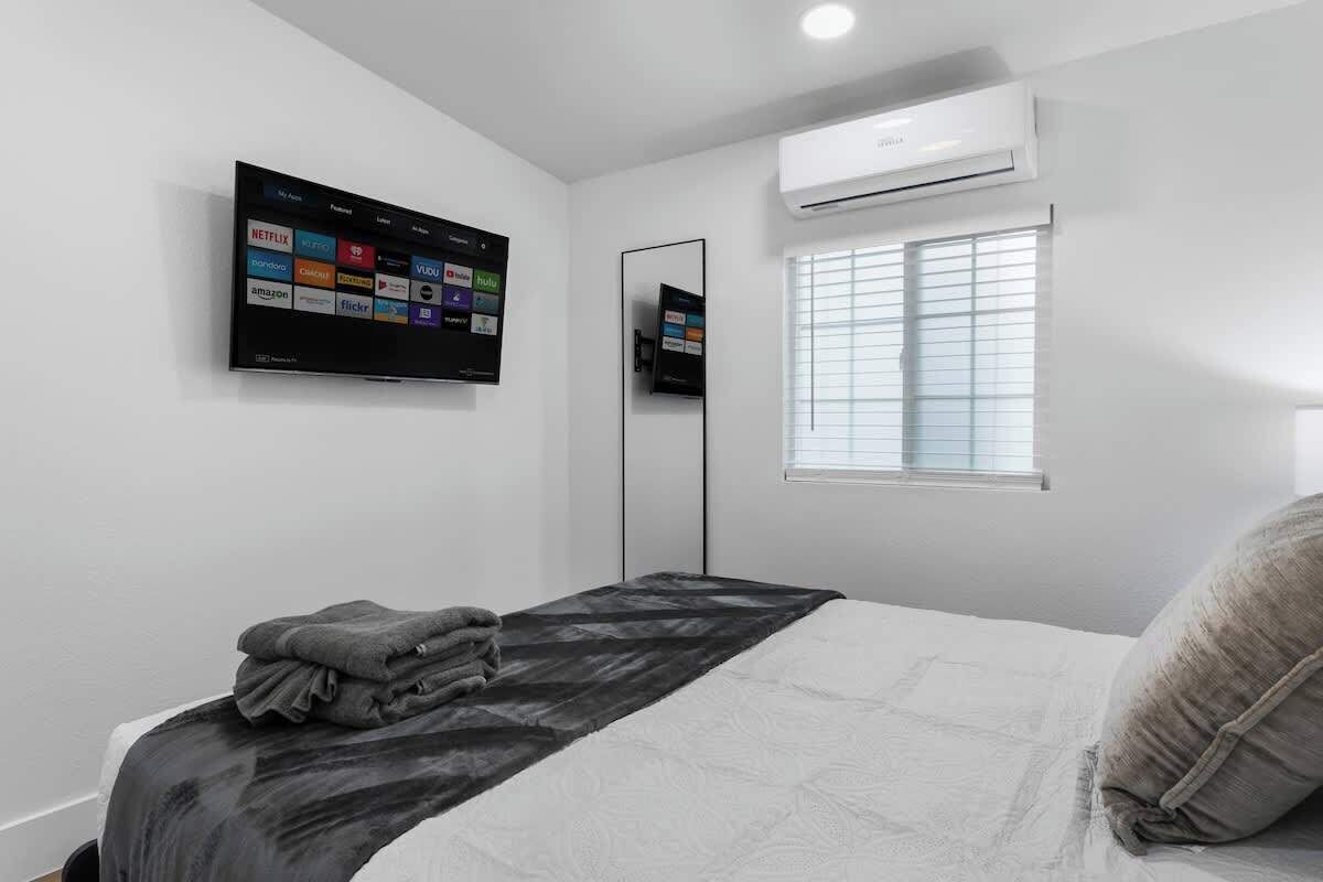 Ein Schlafzimmer mit einem Bett, einem an der Wand montierten Fernseher, einer Klimaanlage und einem Fenster mit Jalousien.