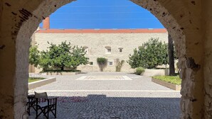 Une entrée en arc donnant sur une cour pavée de pierres, avec un banc et, au fond, un bâtiment doté d’un toit rouge.
