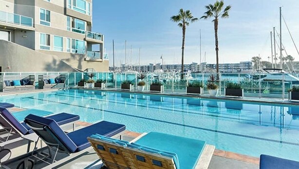 A rooftop pool with lounge chairs, palm trees, and a view of the marina. - The Grace Bay' Private Rooftop Penthouse Water Views Retreat Pool Sauna and Gym (Marina del Rey)