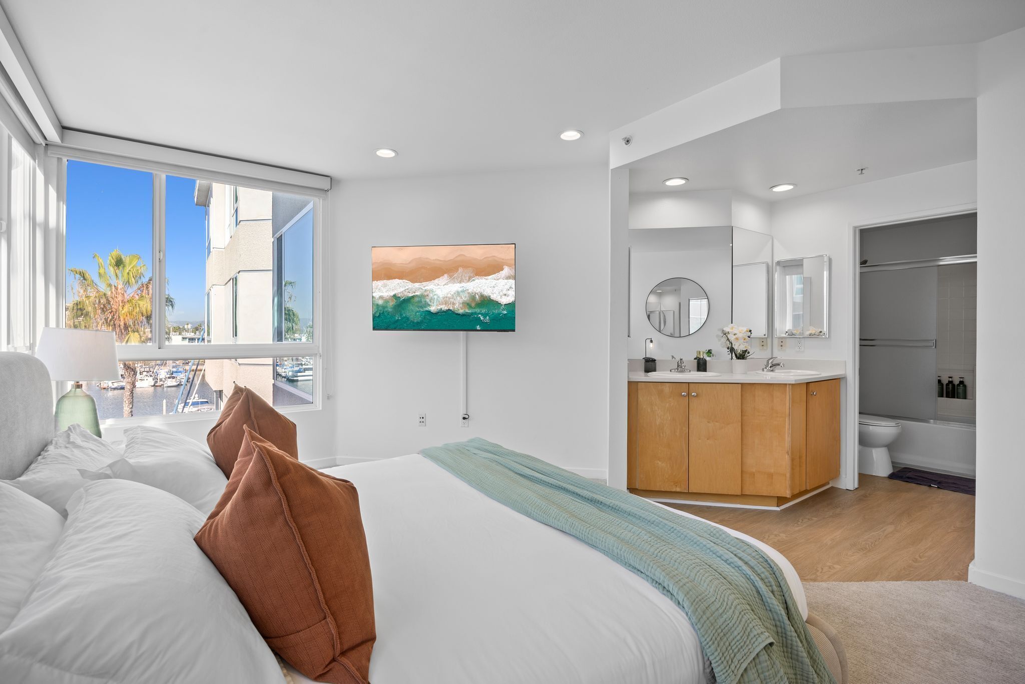 A modern hotel room with a large bed, a TV, a bathroom, and a view of the marina.