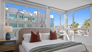 A bedroom with a large bed, two bedside tables, and a view of buildings and palm trees. - The Grace Bay' Private Rooftop Penthouse Water Views Retreat Pool Sauna and Gym (Marina del Rey)