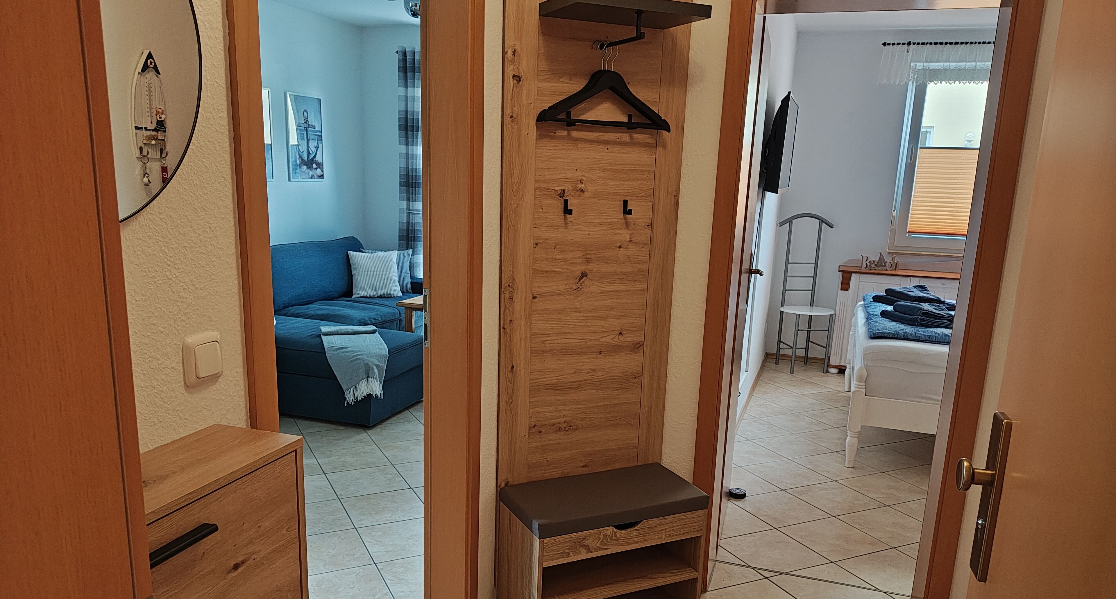 A hallway leading to a bedroom with a wooden wardrobe, a blue sofa, and a small table with a lamp.