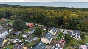Vista aérea de una zona residencial con casas, un fondo forestal y una masa de agua a lo lejos.