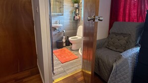 A compact living space with a visible bathroom, a bed, and a seating area. - Room-king Size - Ensuite Room (London)
