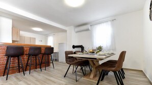 A modern dining area with a wooden table and chairs, a brick accent wall, and a kitchen in the background. - Four Bedroom Villa With Hot Tub (Pasman)