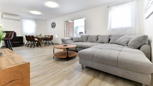 A modern living room with a grey sectional sofa, a wooden coffee table, and a dining area with a table and chairs. - Four Bedroom Villa With Hot Tub (Pasman)