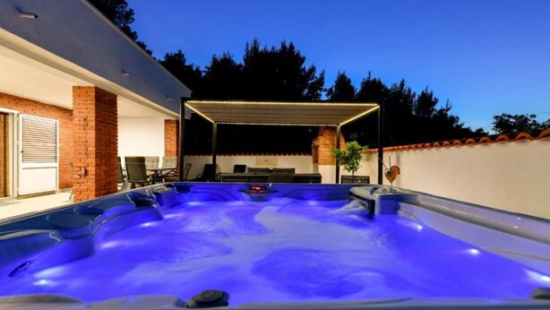 A hot tub with a covered seating area, a brick wall, and a door. - Four Bedroom Villa With Hot Tub (Pasman)
