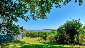 A grassy outdoor area with a view of the sea and hills in the background. - Holiday Home by UK Coast with Sea Views (Great Thorness)