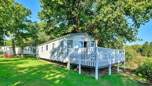 A white mobile home with a porch and a small deck, surrounded by trees and grass. - Holiday Home by UK Coast with Sea Views (Great Thorness)