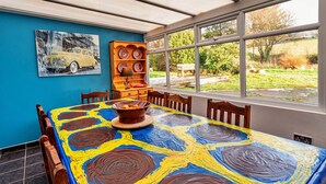 A dining area with a table covered in a colorful abstract painting, a wooden sideboard with plates, and a painting of a car on the wall.