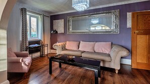 A living room with a sofa, armchair, and coffee table. There is a large mirror on the wall and a chandelier.