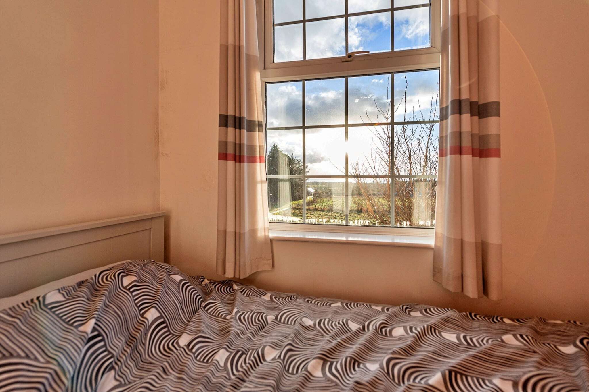 Ein Zimmer mit Bett, einem fensterbehangenen Fenster und Blick nach draußen.