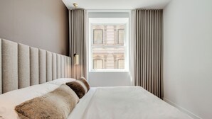 A neatly made bed with a headboard, a window with curtains, and a wall-mounted light fixture. - Luxury two bedroom corner unit - Old Montreal - Parking Included (Montréal)