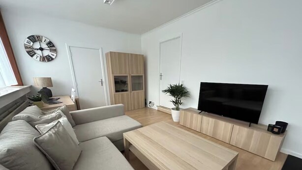 A modern living room with a beige sofa, a wooden coffee table, a flat-screen TV, and a wall clock.