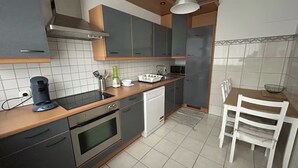 A modern kitchen with grey cabinets, a wooden countertop, a coffee maker, a dishwasher, and a dining area with a white table and chairs.