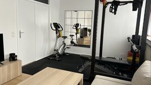 A compact room with a wooden table, a stationary bike, a mirror, and a weight bench.