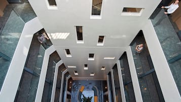 A modern interior with a central atrium, geometric ceiling design, and a seating area with a plant.