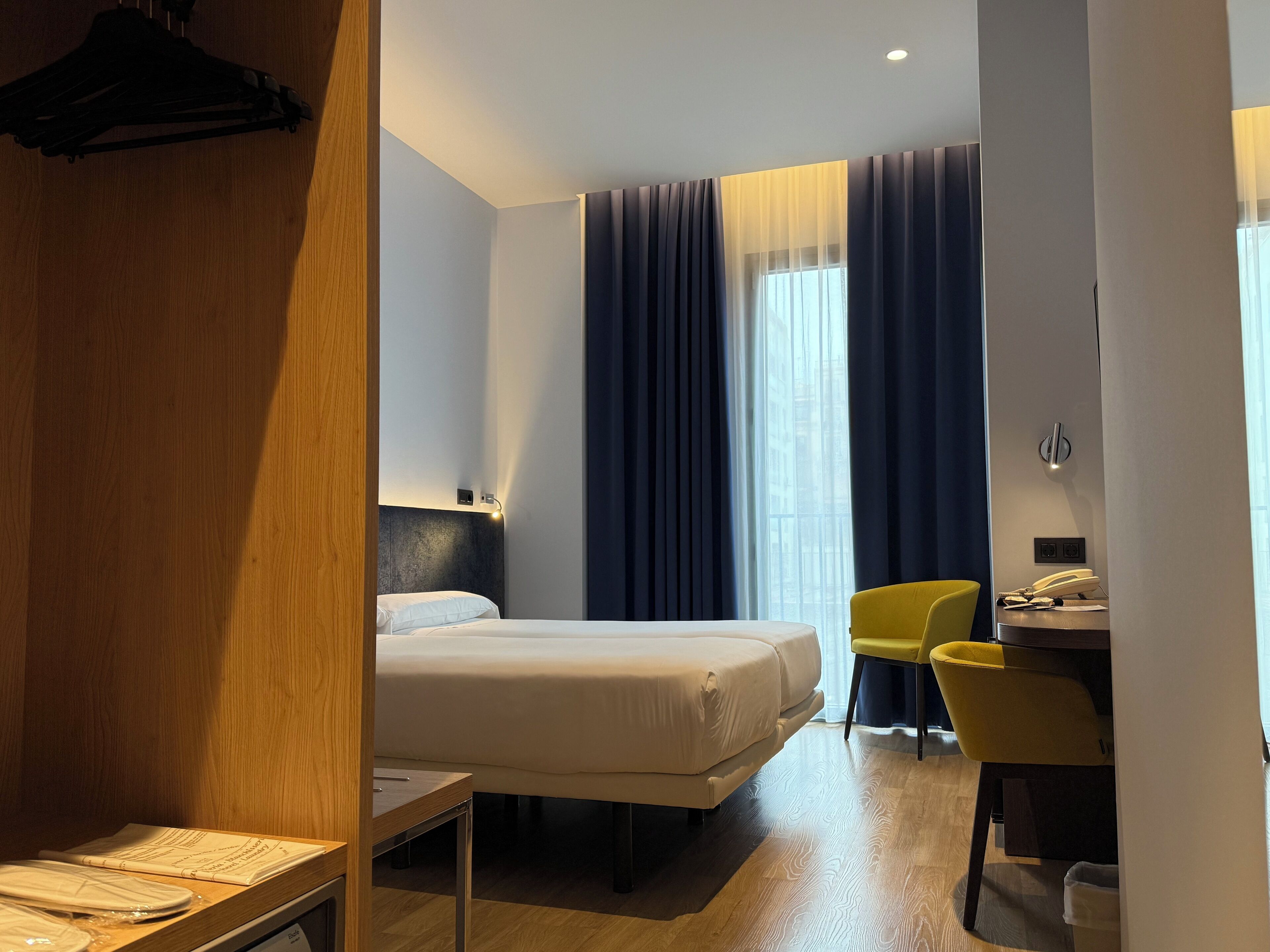 Una habitación de hotel con una cama, un escritorio con una silla y una ventana con cortinas.