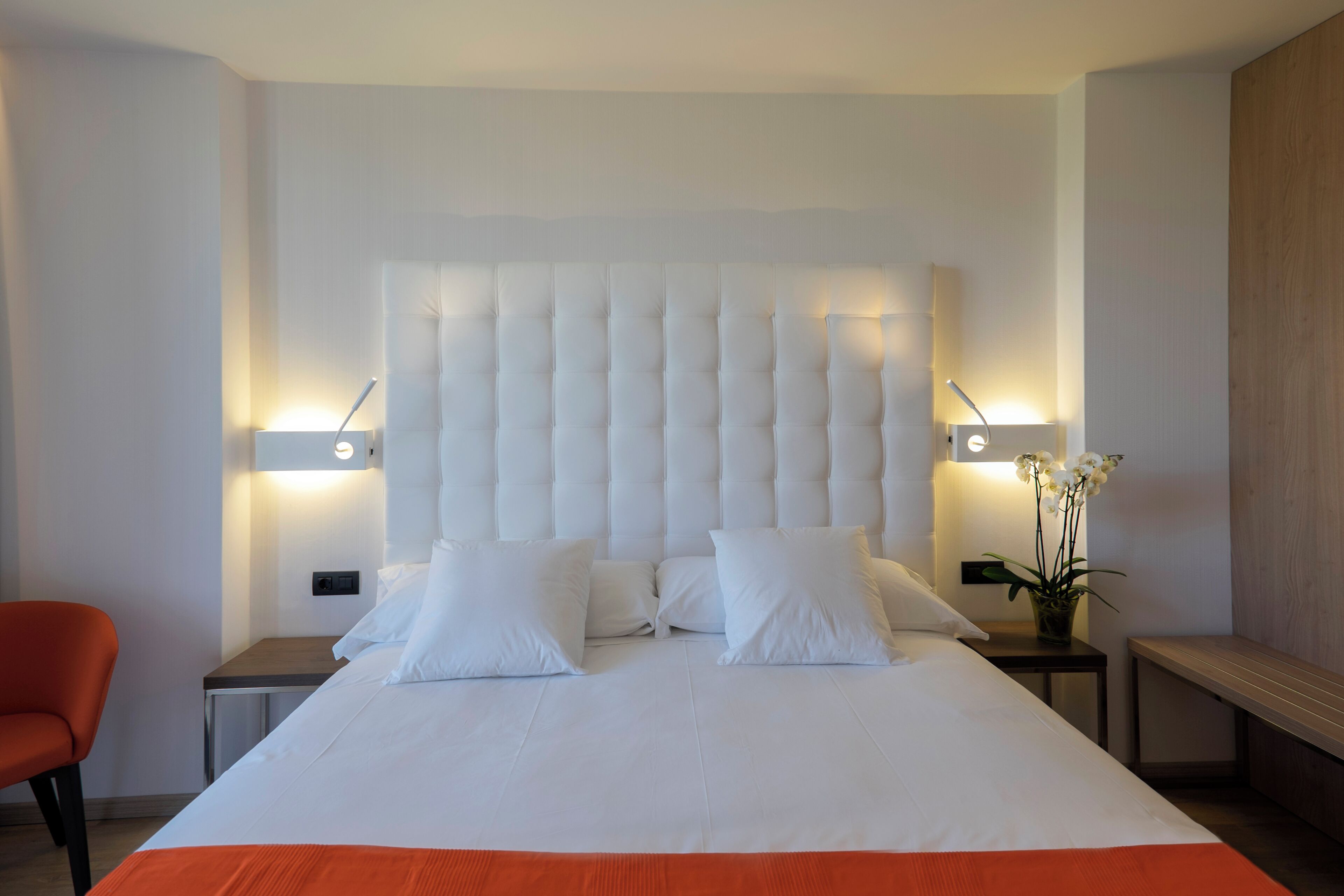 A modern hotel room with a large bed, two bedside tables, a chair, and a bench.