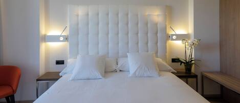 A modern hotel room with a large bed, two bedside tables, a chair, and a bench.