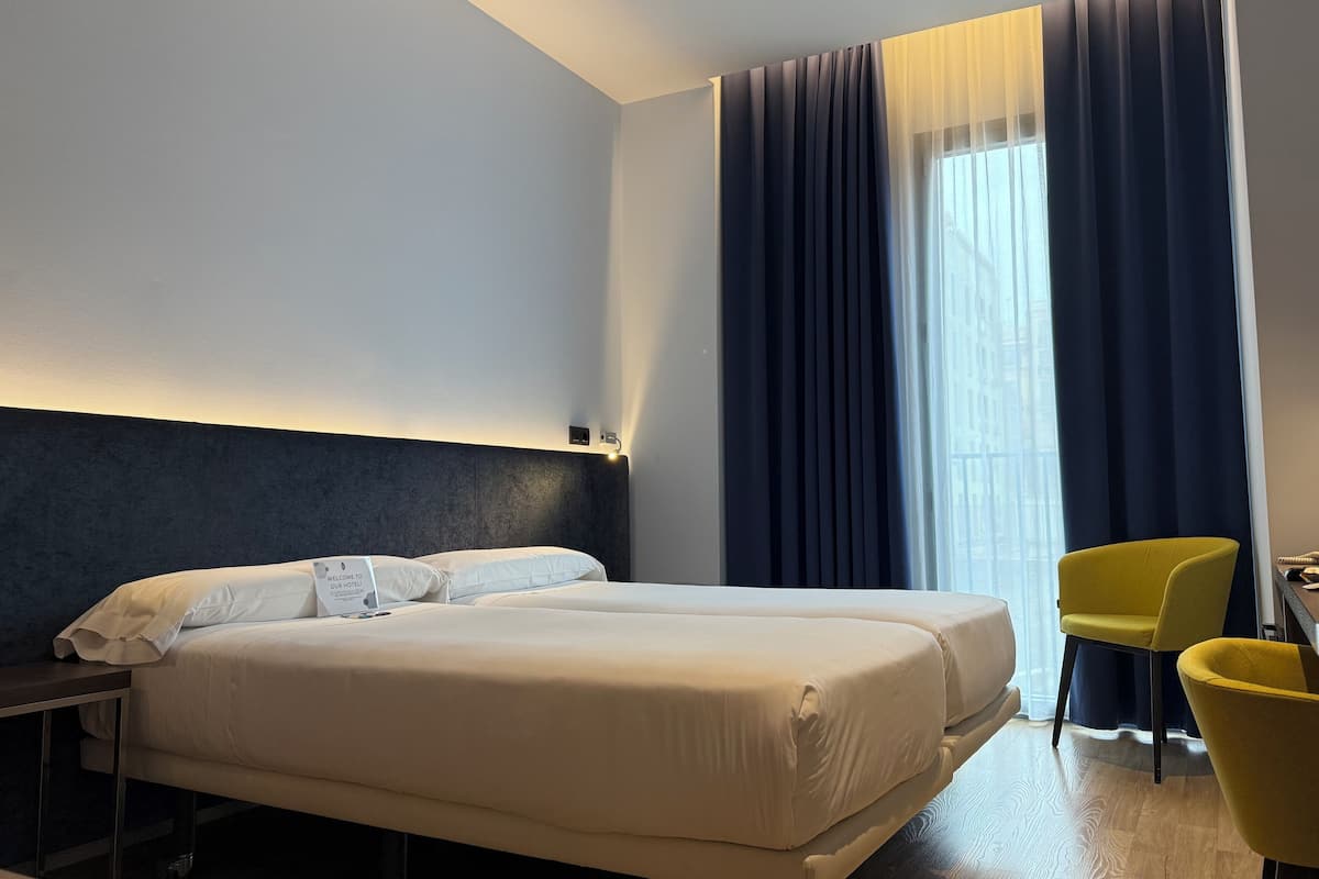 A hotel room with a large bed, a desk, a chair, and a window with curtains.