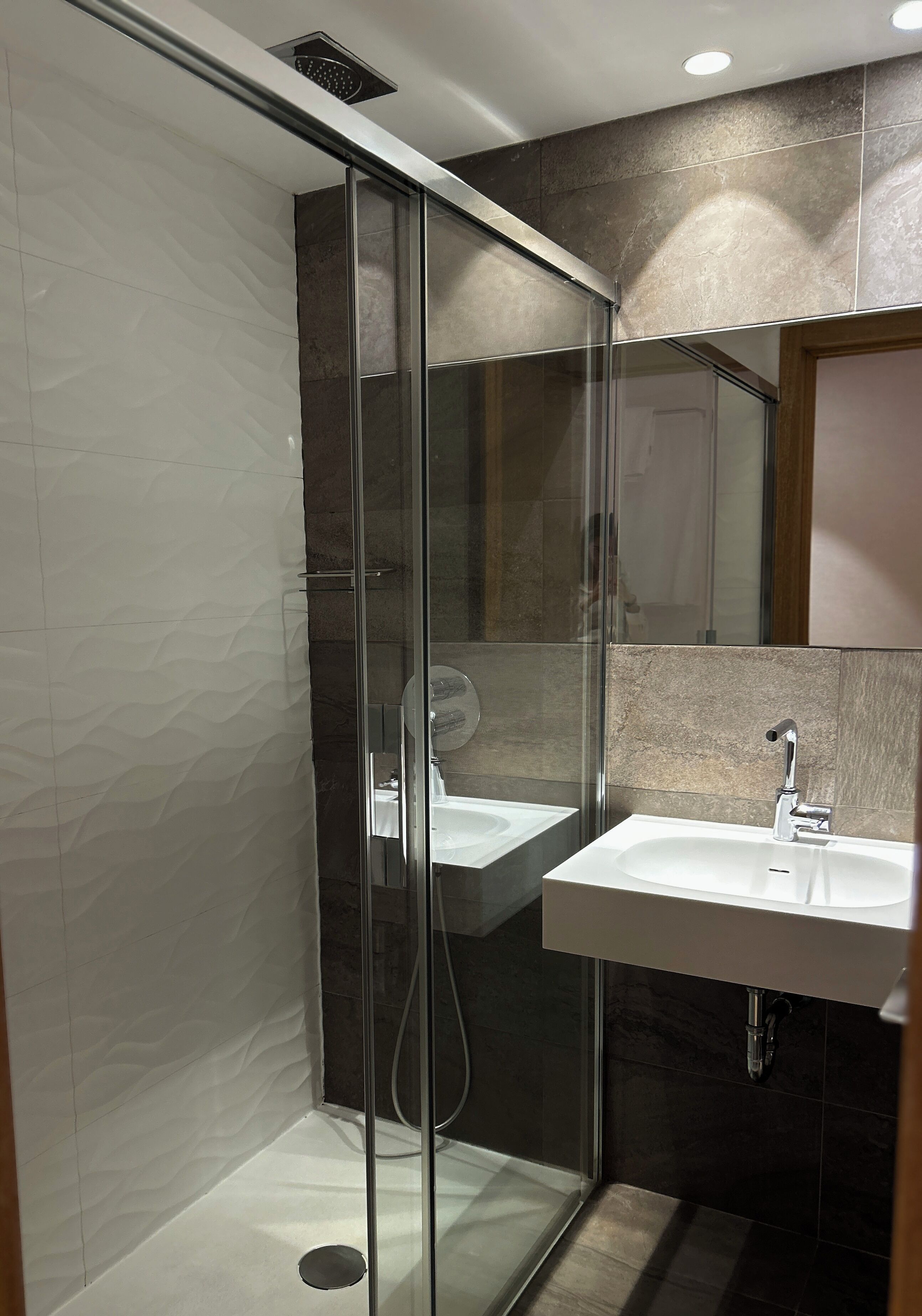 A modern bathroom with a glass-enclosed shower, a white sink, and a mirror above it.