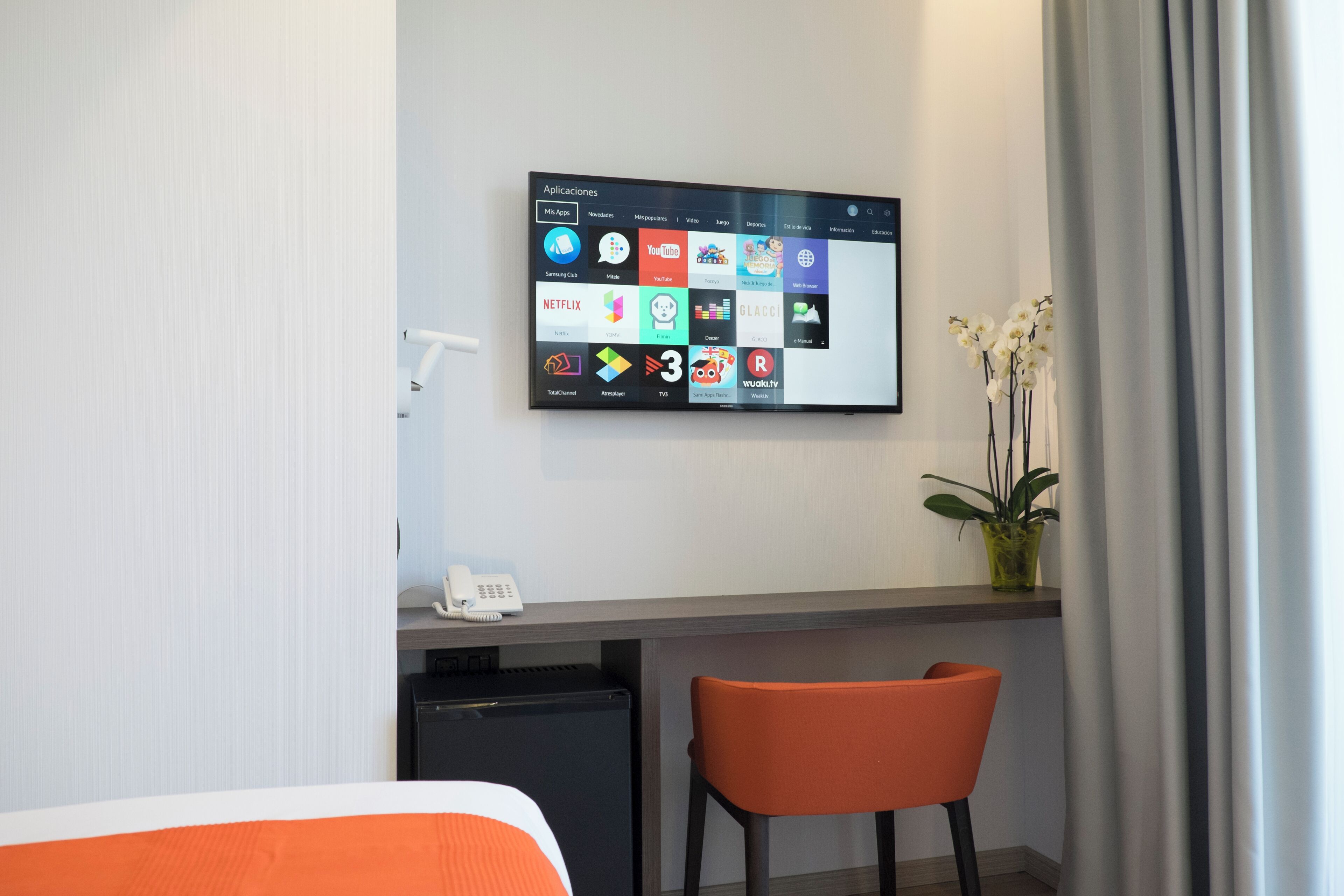 A hotel room with a flat-screen TV mounted on the wall displaying various apps.