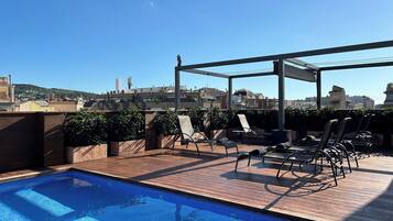 A rooftop pool area with a clear view of the cityscape, including buildings and a hill in the distance.