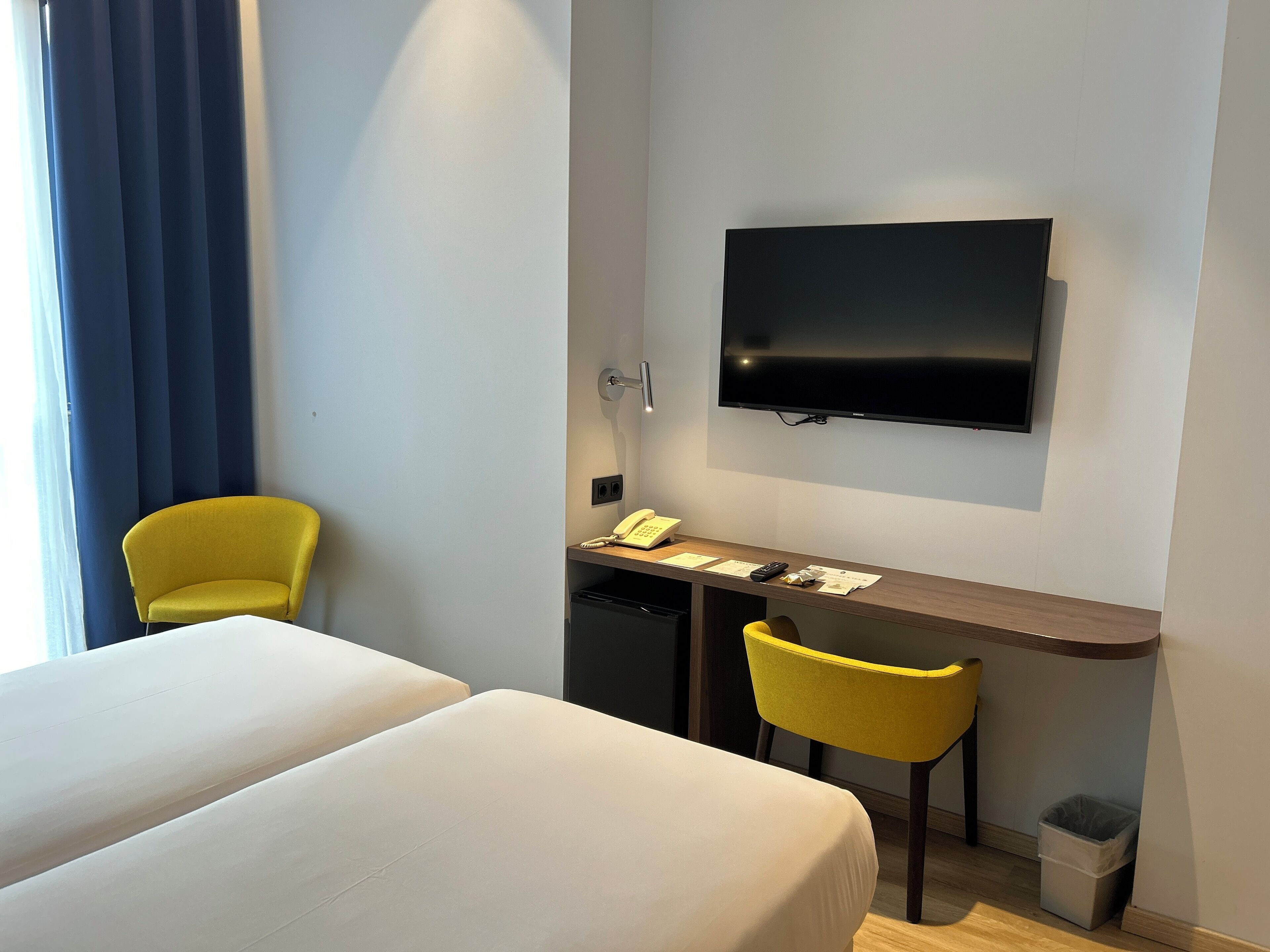 A hotel room with two beds, a desk with a chair, a TV, and a telephone.
